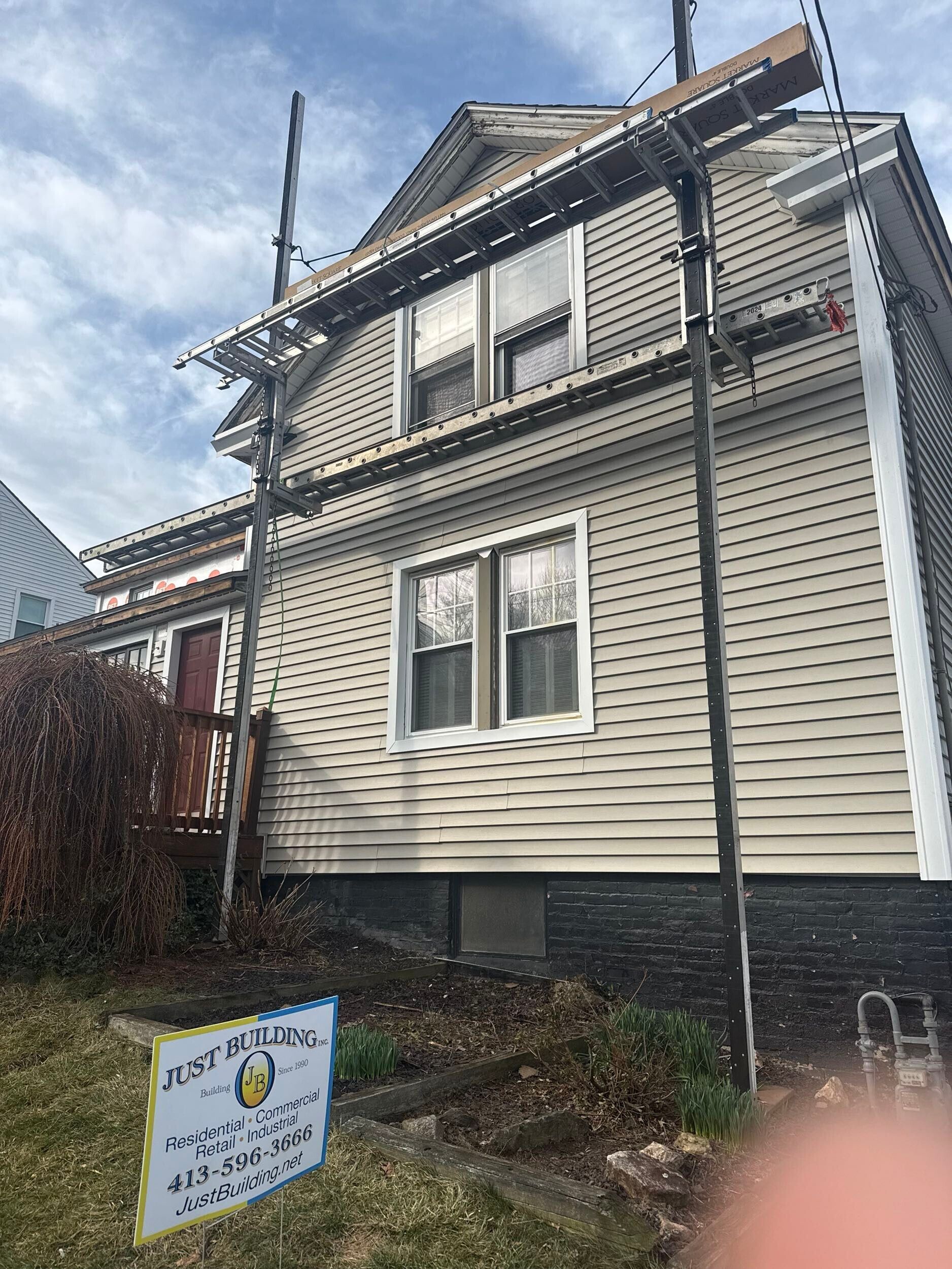 Damaged house exterior with missing roof sections and a sign in the front yard