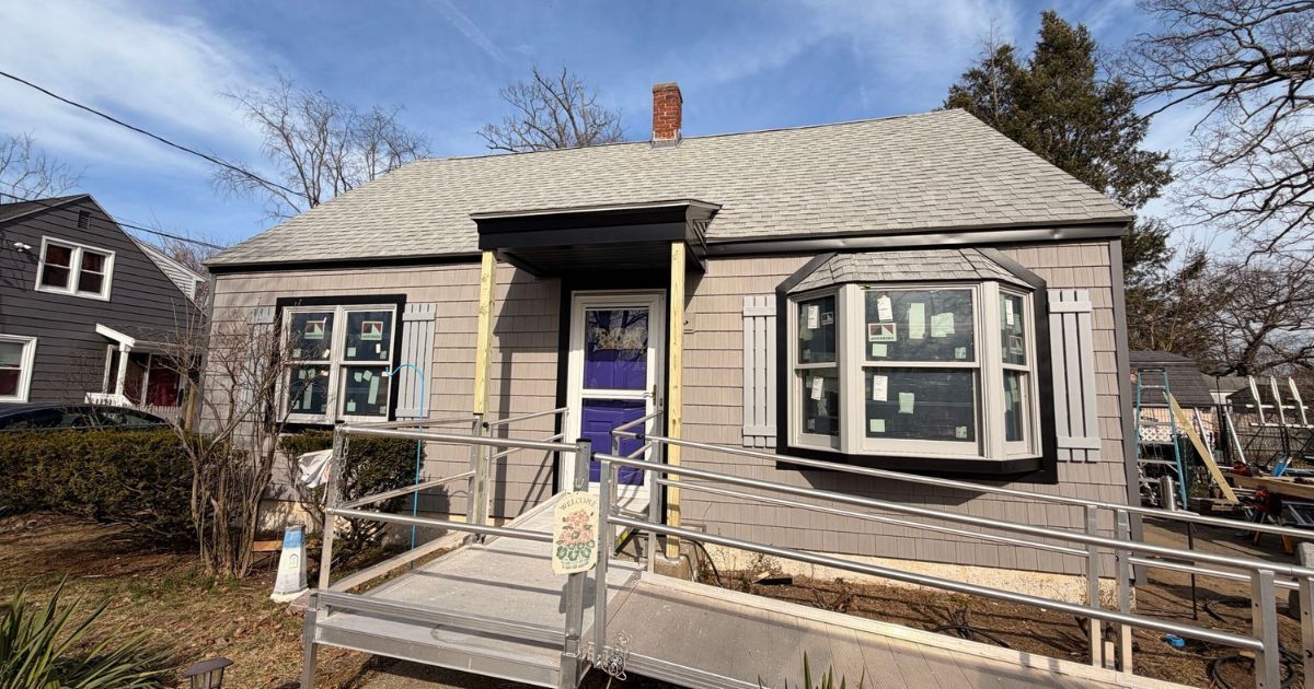 Small gray house with purple front door, front porch ramp, and winter trees in the yard