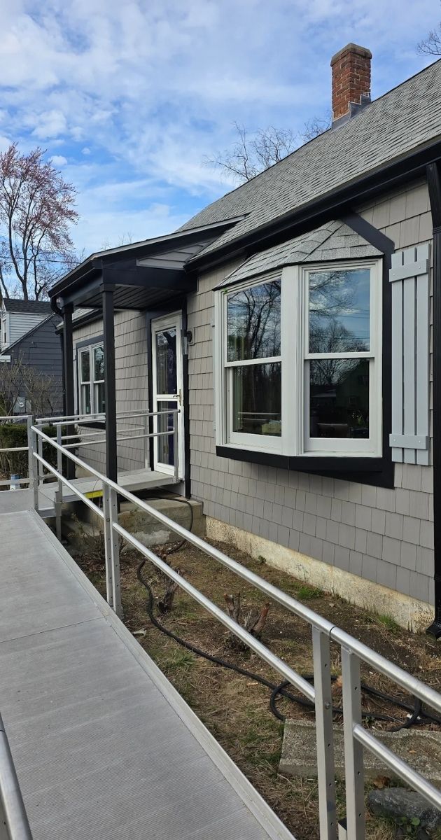 Exterior of a gray house with black-trimmed bay window and wheelchair ramp along the side