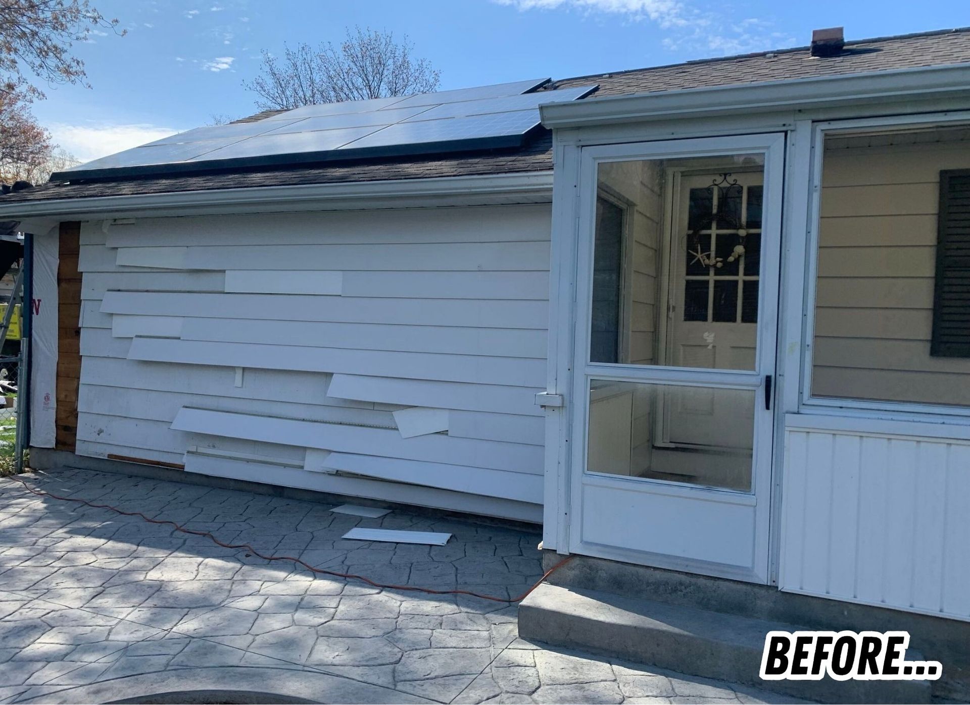 White house exterior with damaged siding beside a front porch and screen door