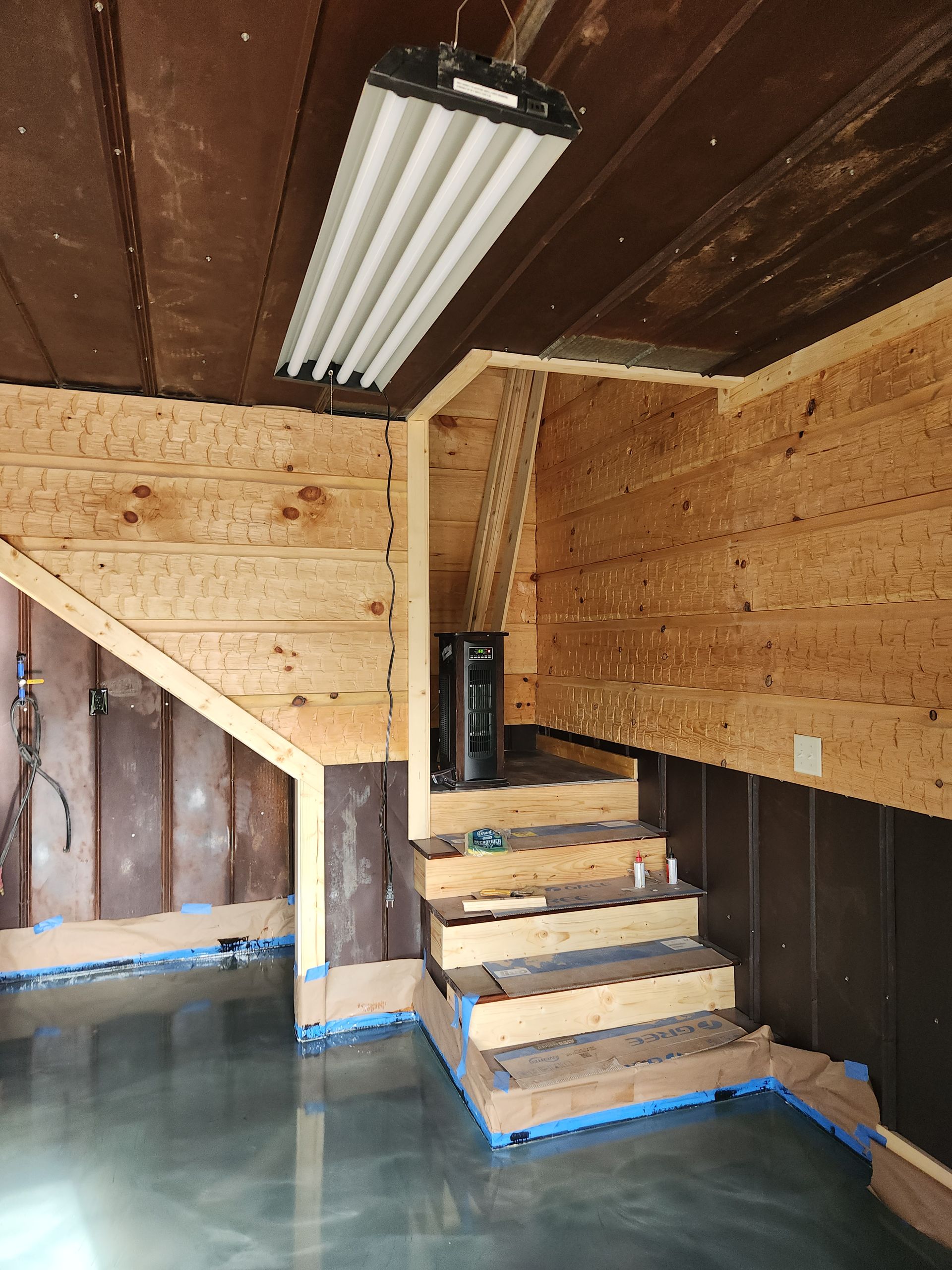 Unfinished interior with wooden stairs under construction, exposed walls, and a fluorescent ceiling light