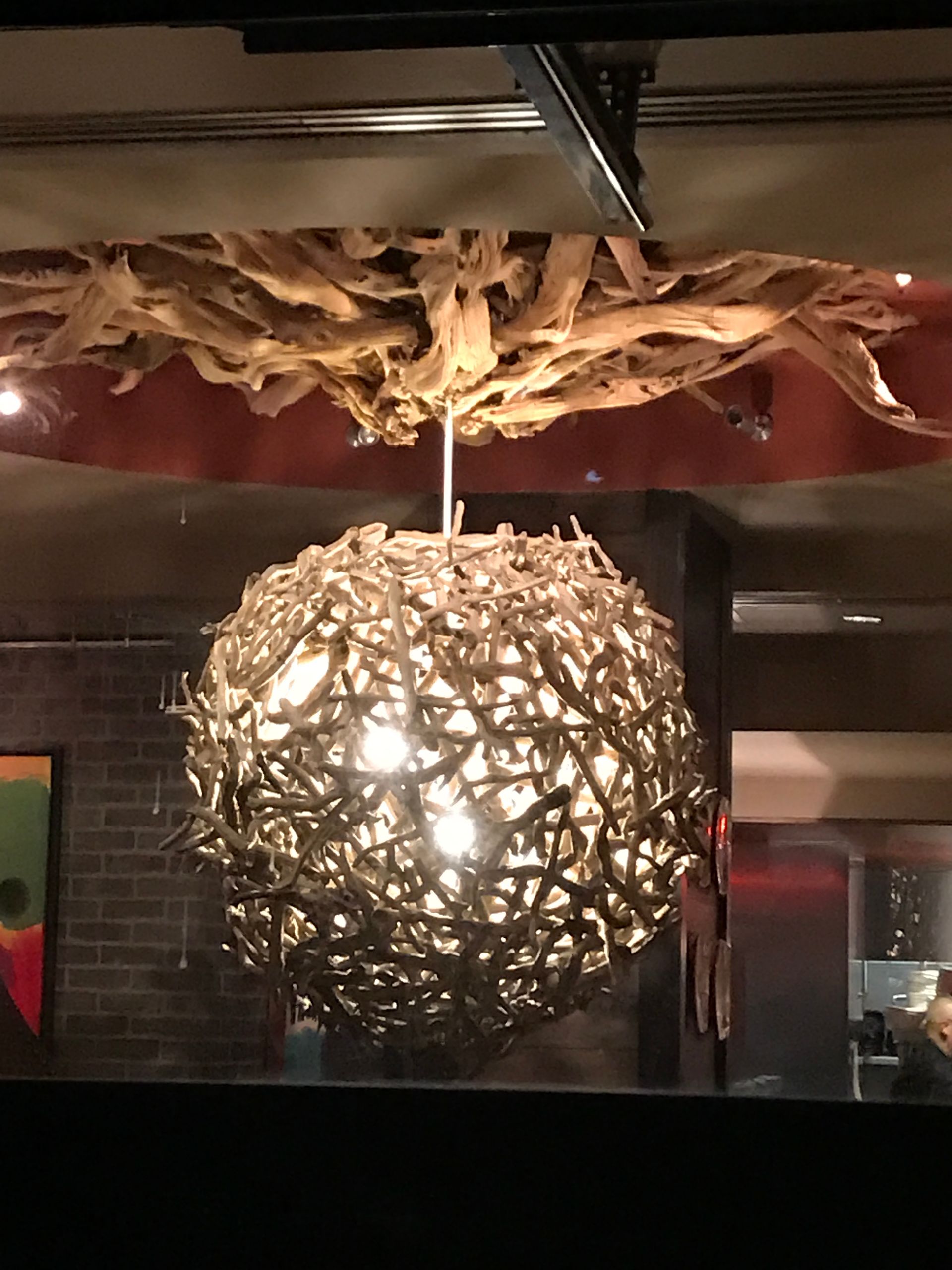 Glowing spherical pendant light made of woven twigs hanging from a rustic ceiling
