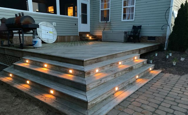 Wooden deck steps with warm orange lights on the risers beside a house at dusk