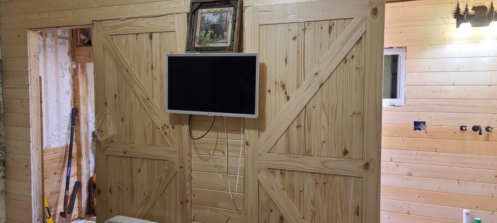 Rustic wood-paneled room with large barn-style doors and a wall-mounted TV in the center.