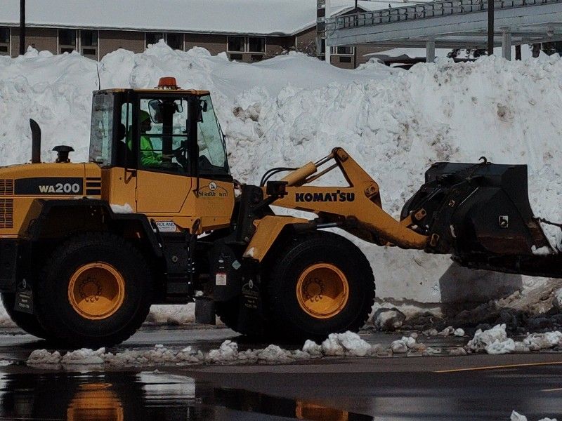 A yellow komatsu wheel loader is parked in front of a pile of snow