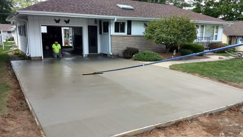 A man is standing in a concrete driveway in front of a house.