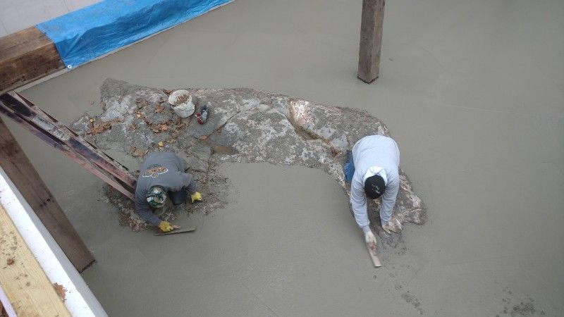 A couple of men are working on a concrete floor.