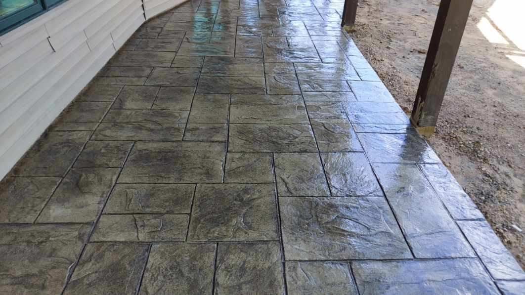 A concrete walkway leading to a house with a brick pattern.