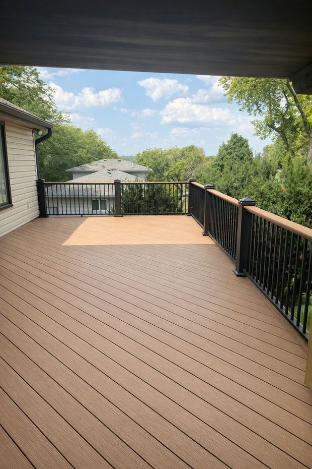 Covered wooden deck with black railings overlooking a green backyard and partly cloudy sky