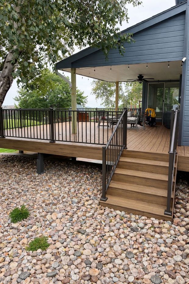 Blue house deck with steps, black railings, and a covered porch over a rock-covered yard.