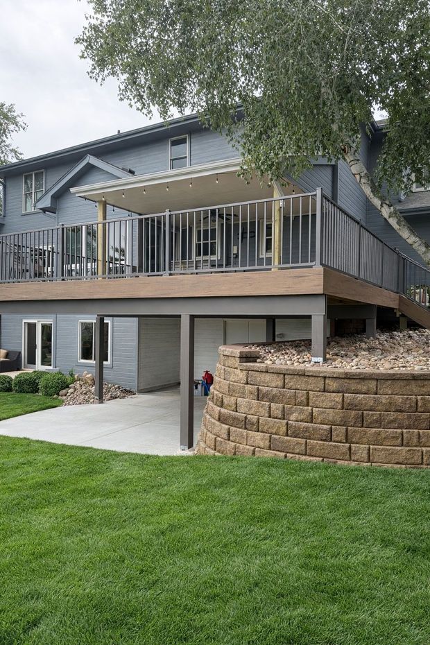 Two-story house with a raised wooden deck, stone retaining wall, and manicured lawn