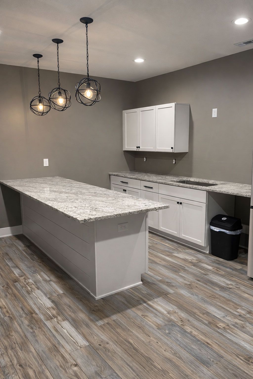 Modern kitchen with gray walls, granite island, white cabinets, and pendant lights over wood-look flooring