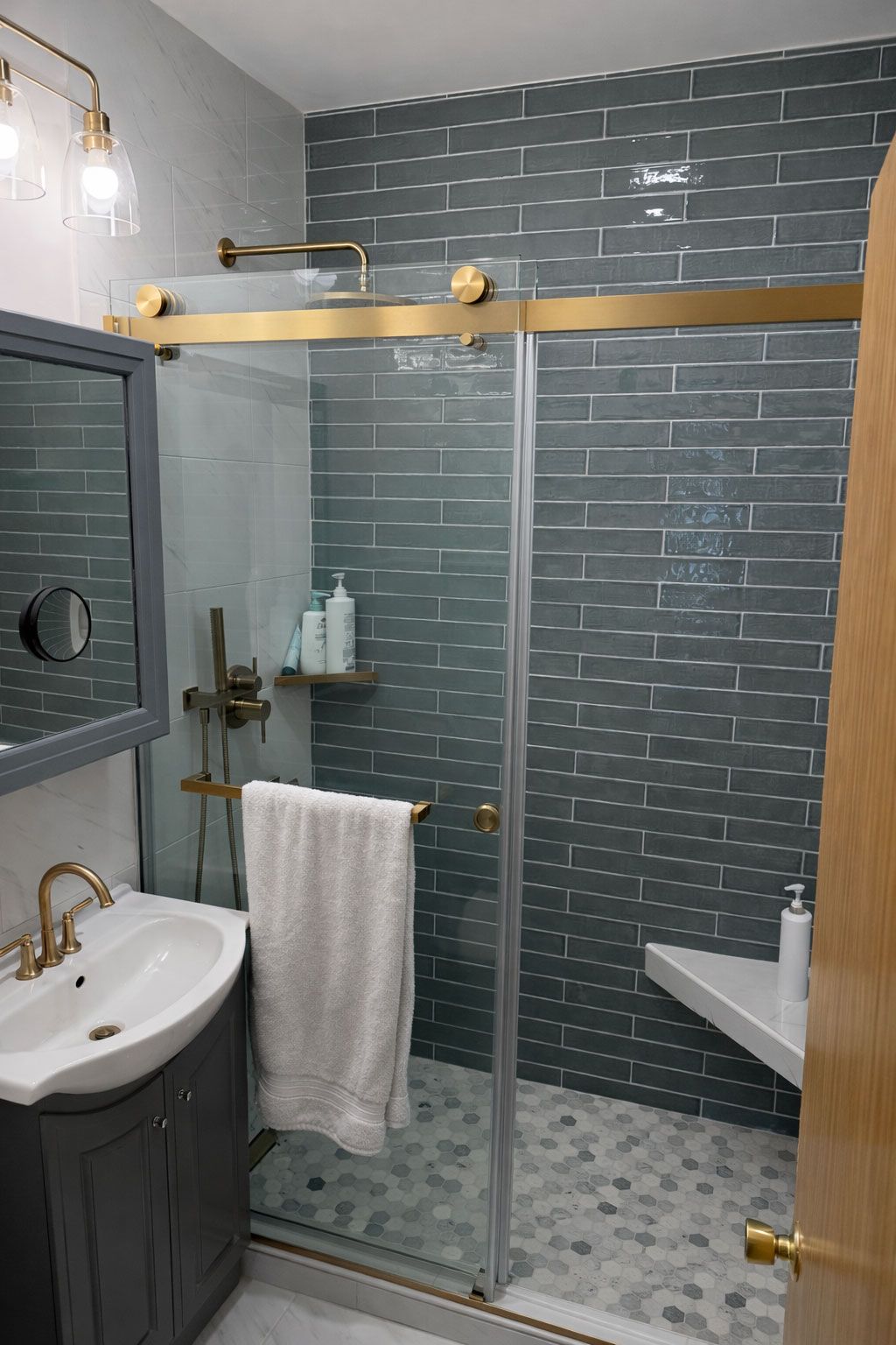 Small bathroom with blue tile shower, glass door, towel rack, sink, and grab bars on walls.