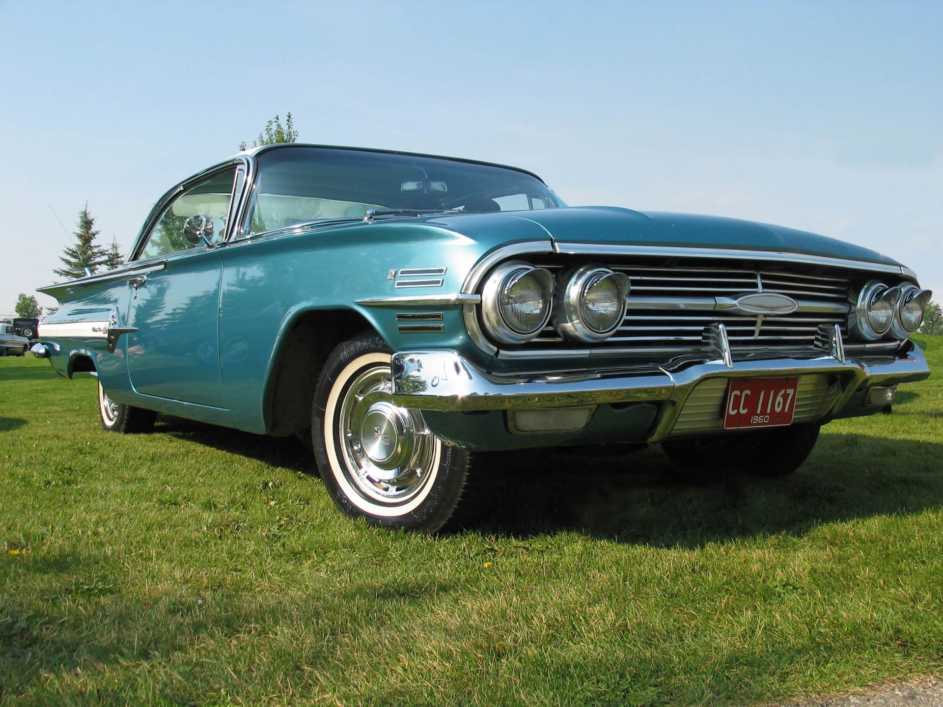 Teal 1960 Chevrolet Impala coupe parked on green grass, white-wall tires, sunny day.