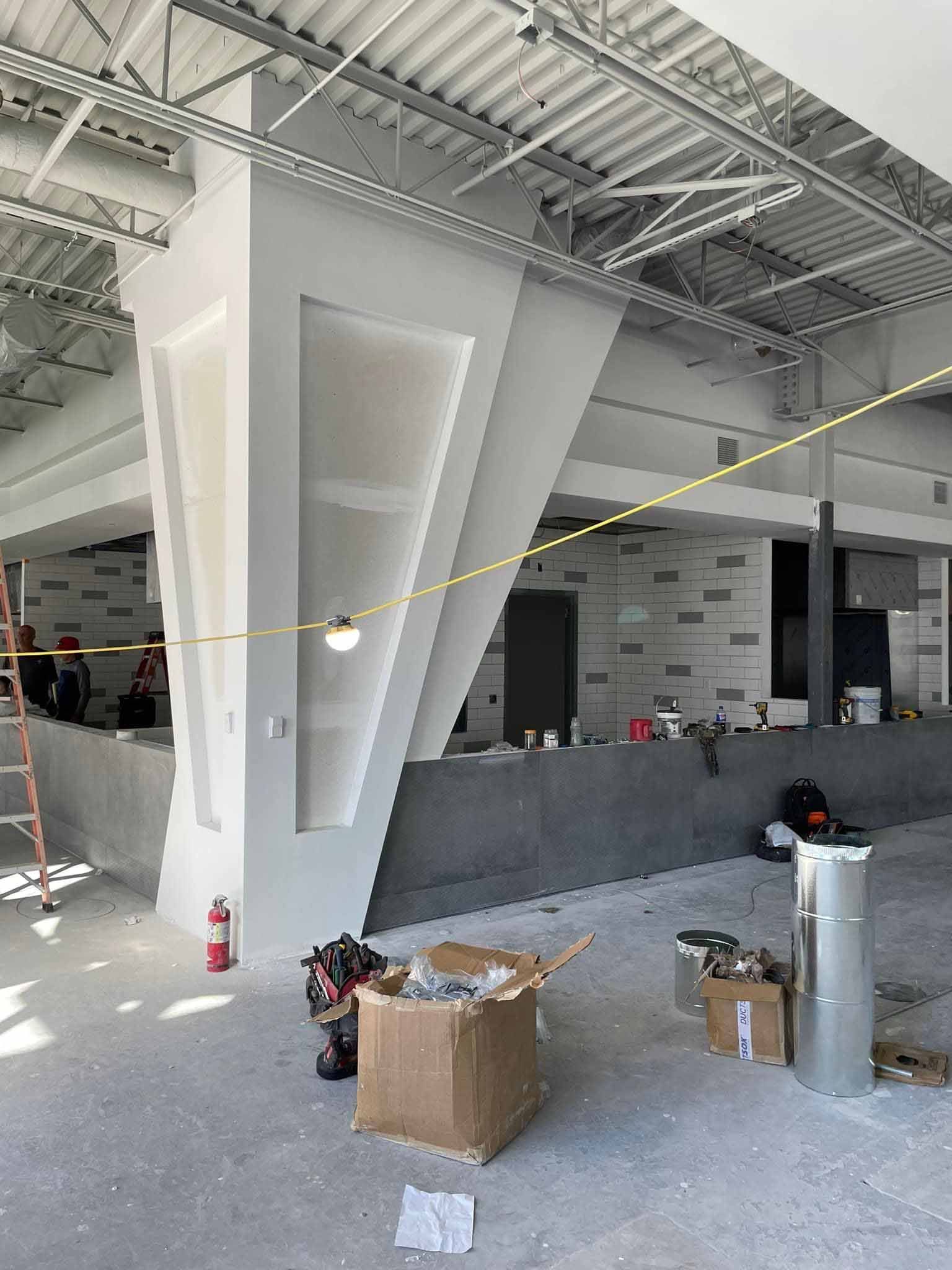 Construction of a modern commercial space with white columns, gray walls, and exposed ceiling beams.