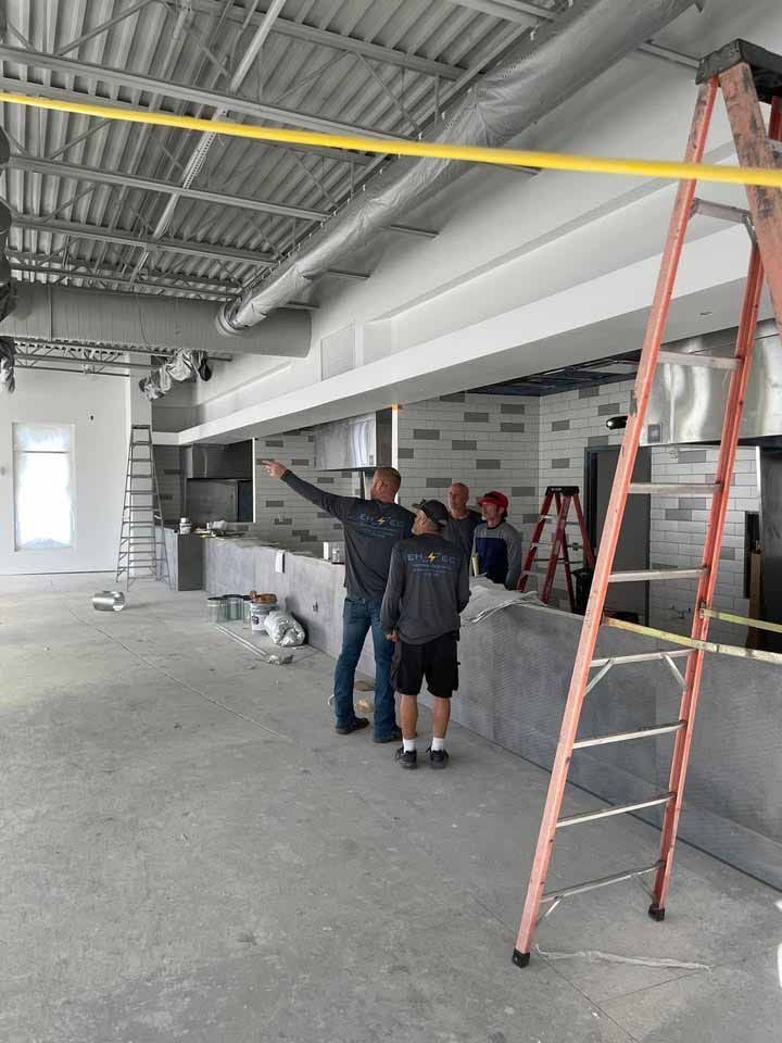 Construction site interior. Four men assessing a long counter. Red ladder is present.