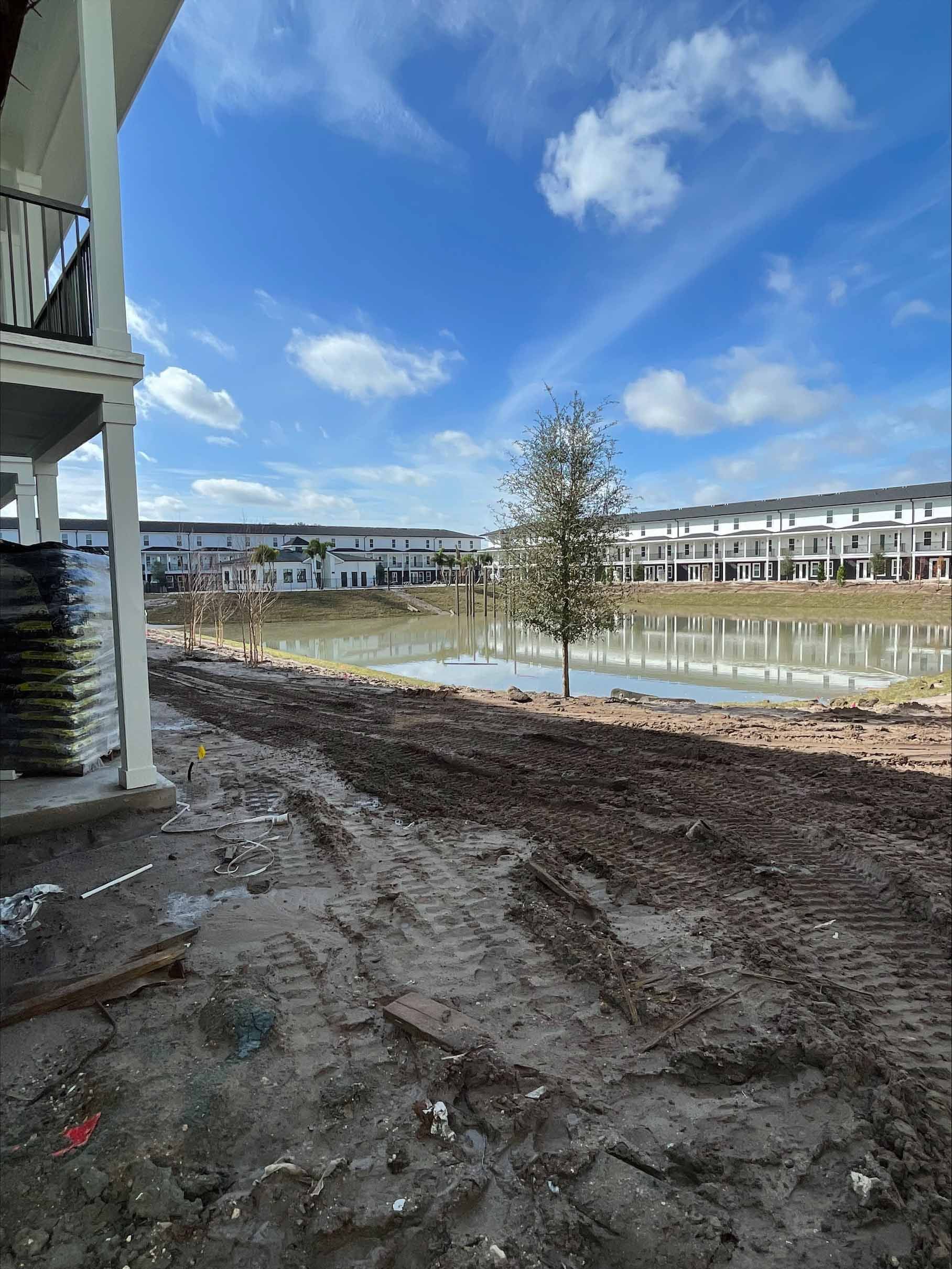 Muddy construction site with lake, buildings, and blue sky.