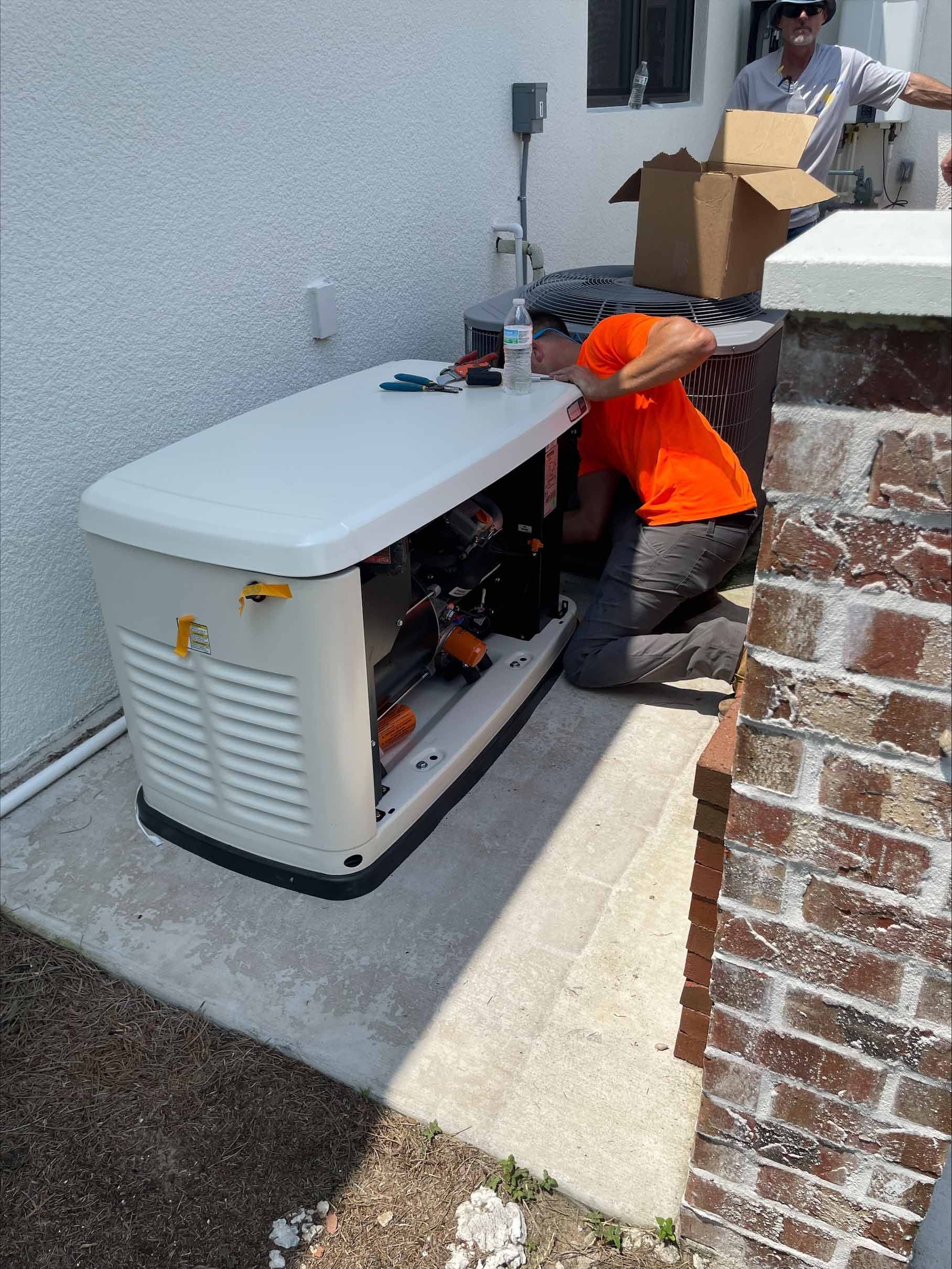 Two men installing a beige generator near a brick pillar. One man works inside, the other by a cardboard box.