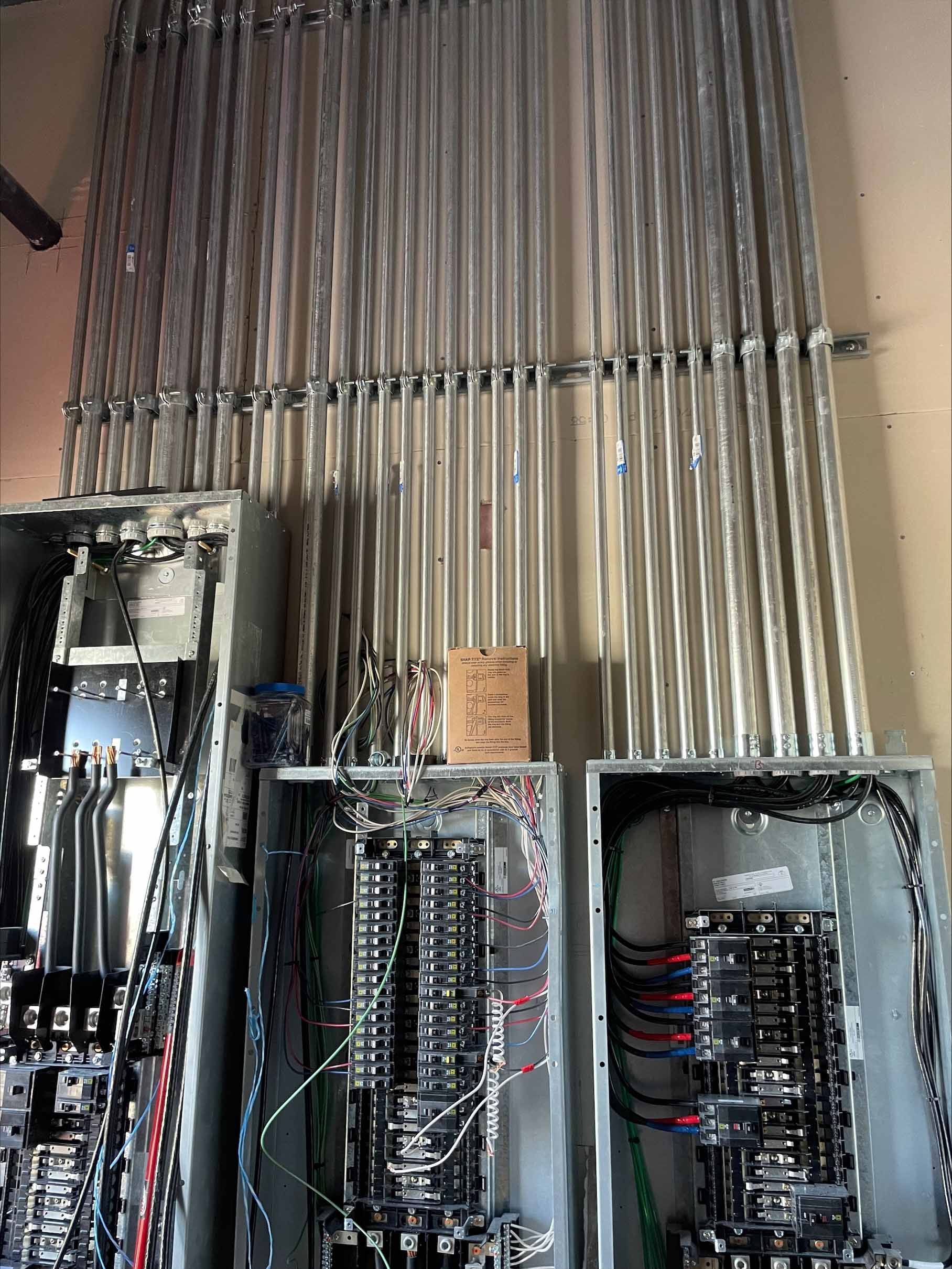 Electrical panels with conduit running above them against a wall.