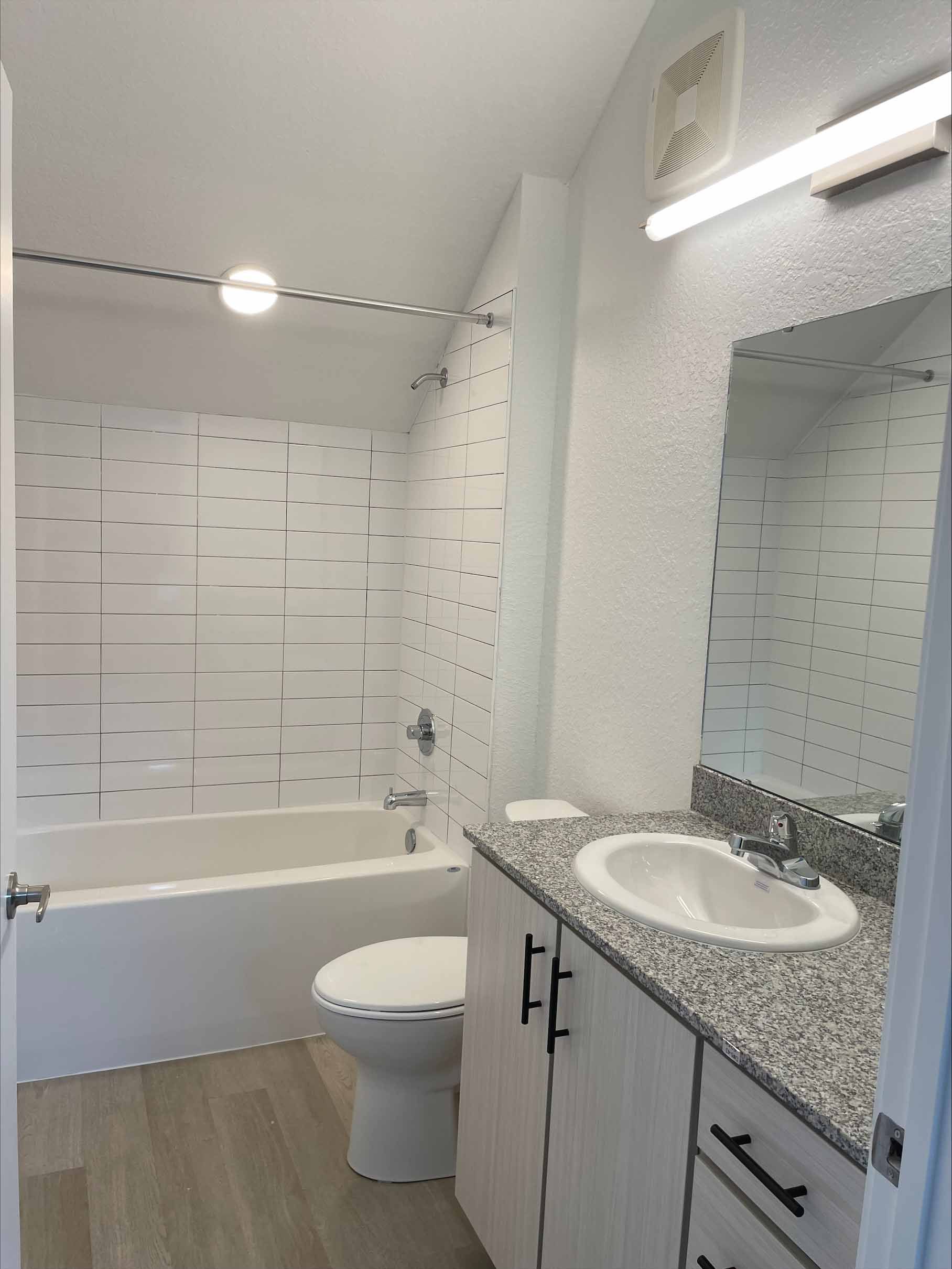 Bathroom with white tub, toilet, sink, granite countertop, and black accents.