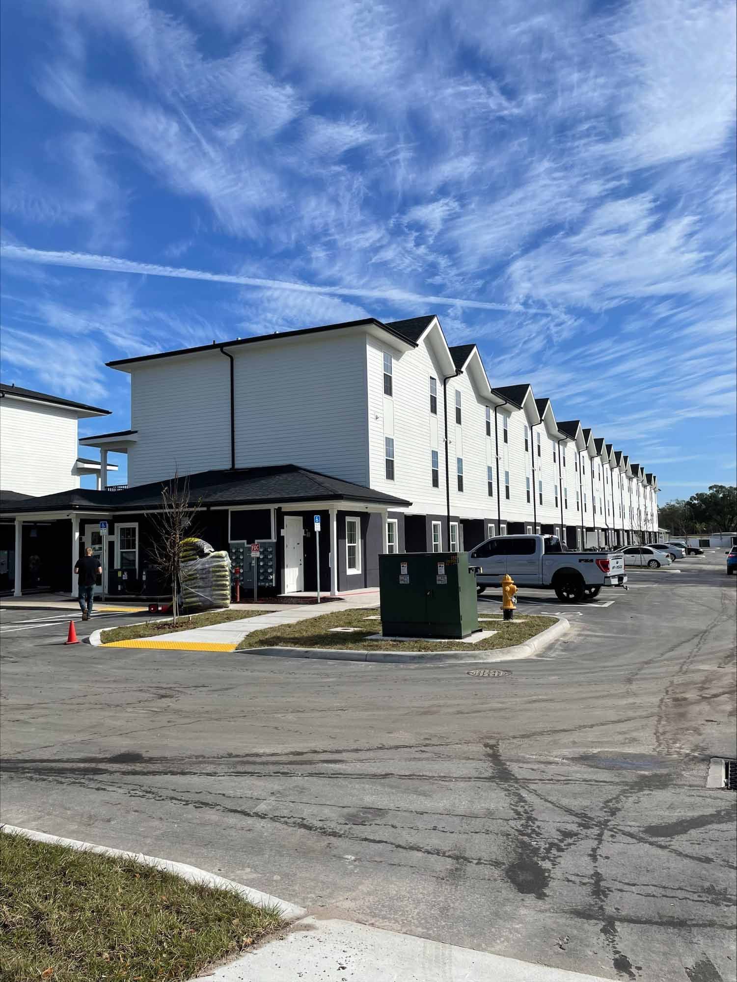 Multi-story white apartment building with black trim, sunny blue sky.