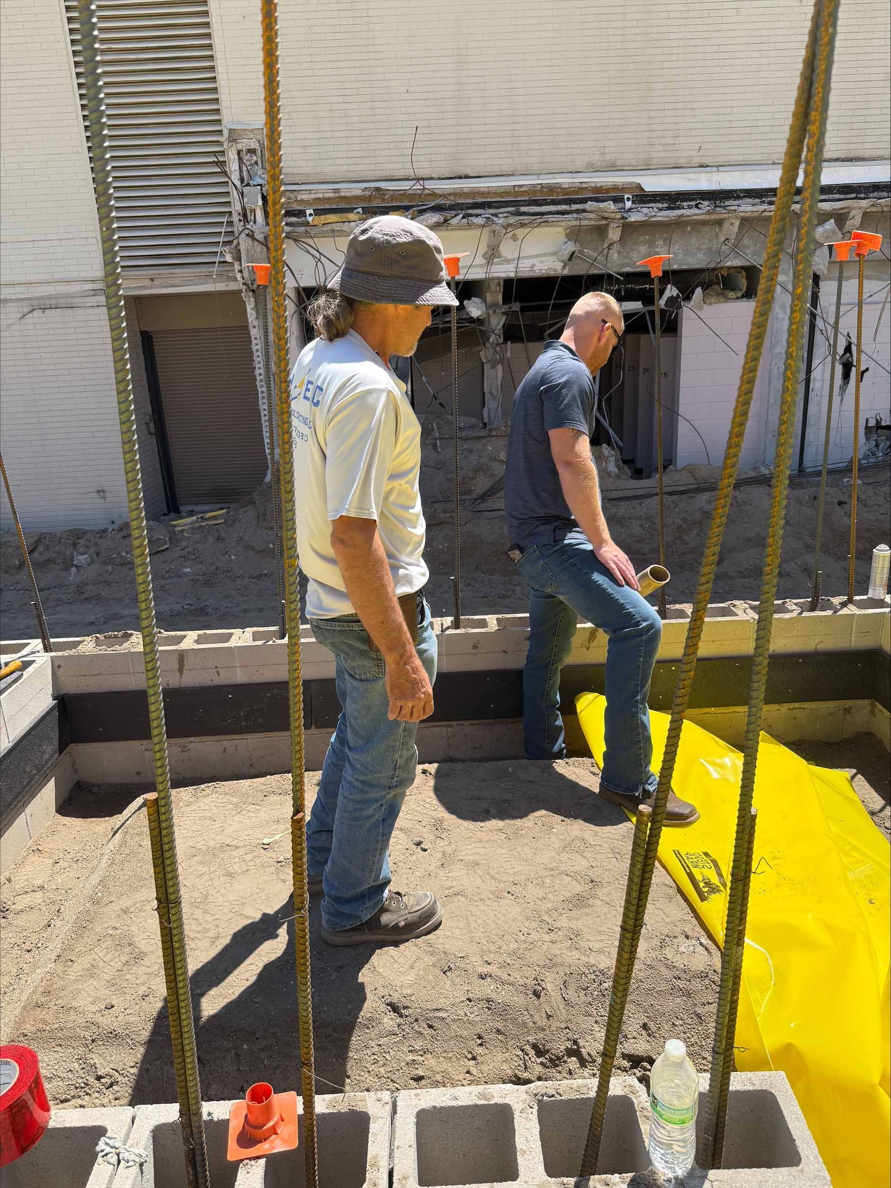 Two men standing at construction site with rebar and cinder blocks.