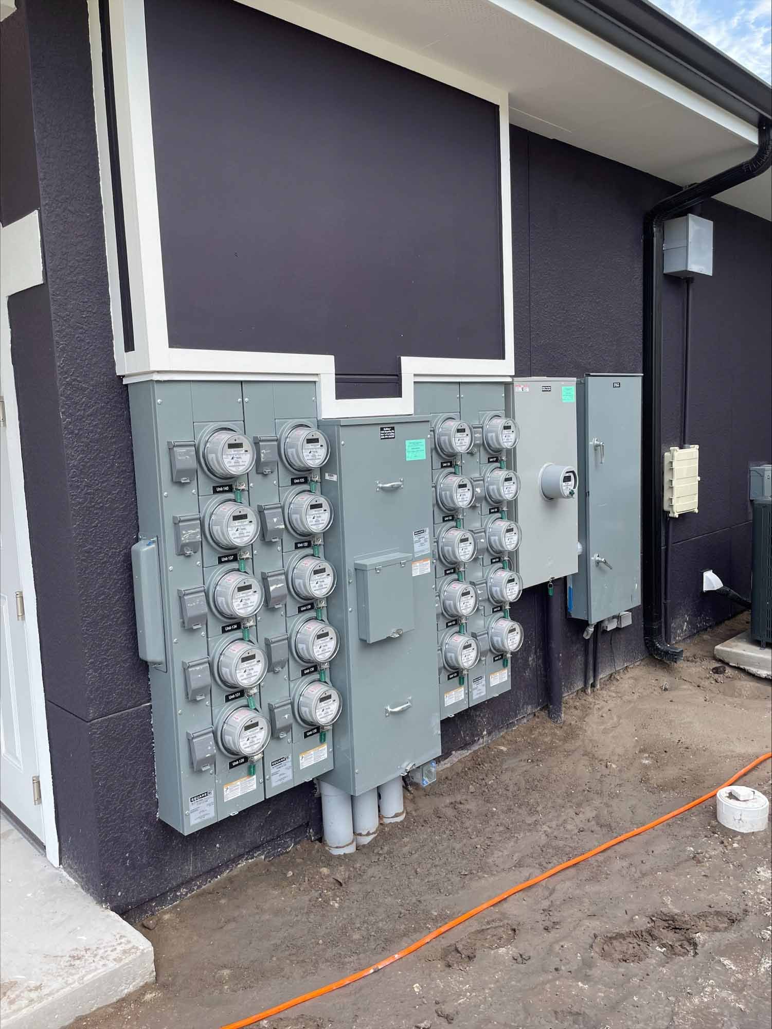 Electrical meters and boxes mounted on a dark building exterior with a white trim.