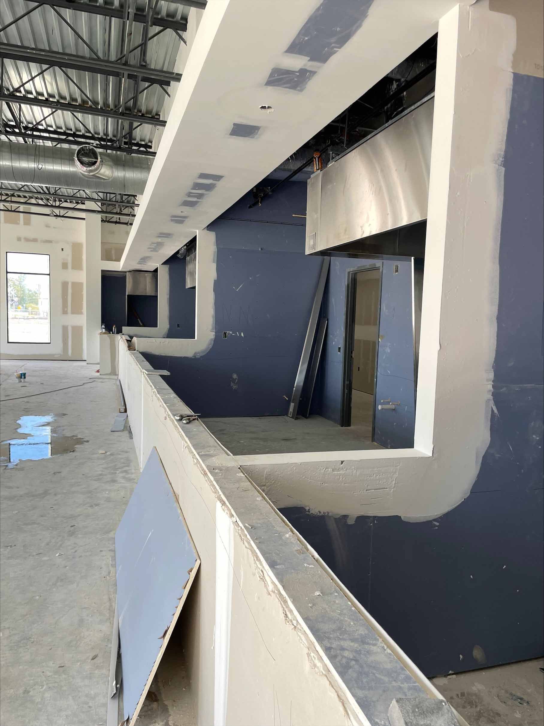 Construction site: drywall bar with openings, gray walls, white trim, metal ceiling.