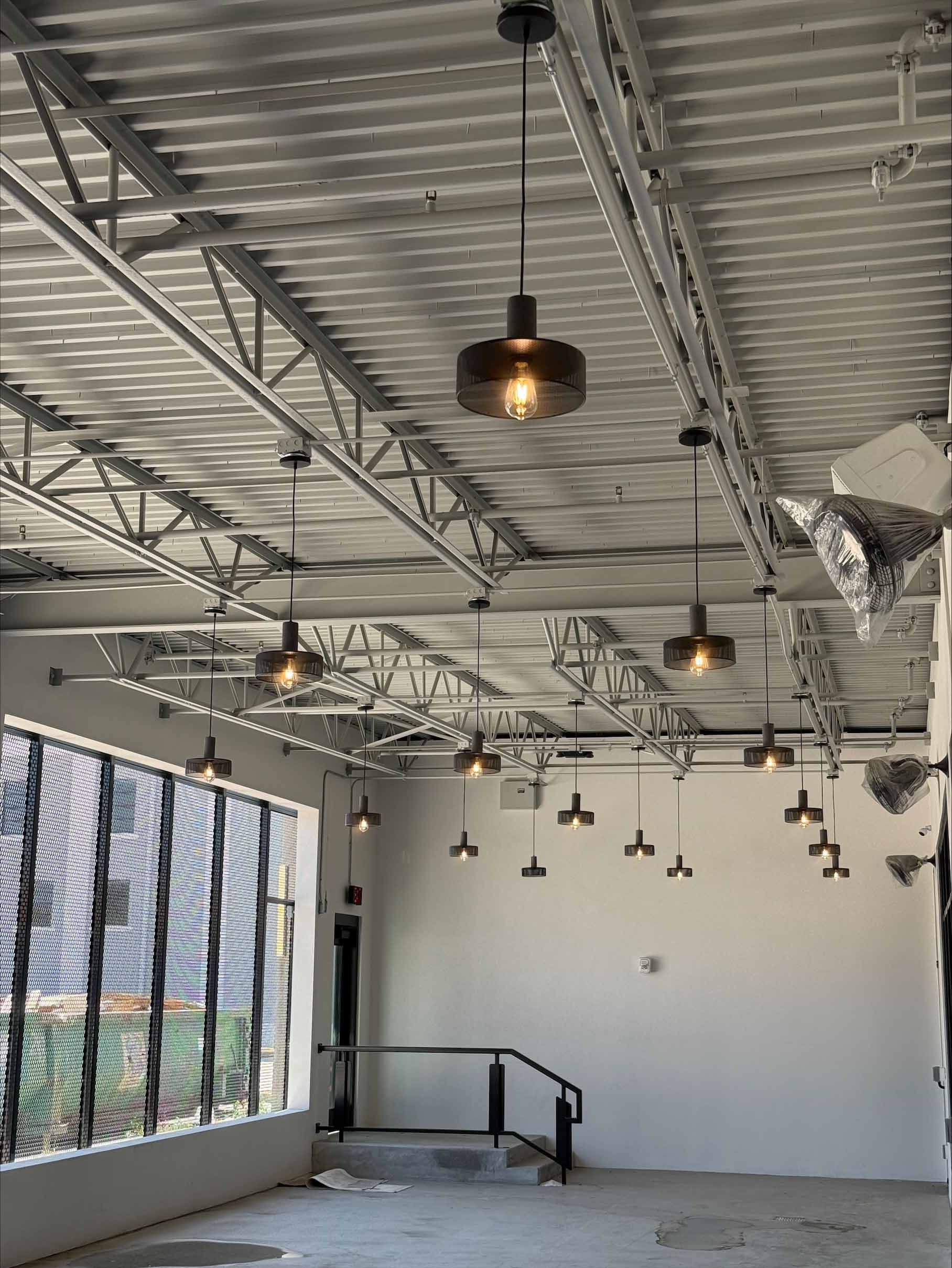 Interior view of a room under construction with pendant lights hanging from a metal ceiling.