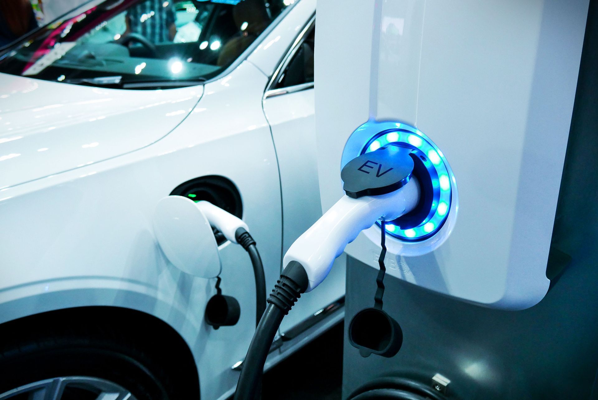 White electric car being charged at a charging station; charging cable plugged in, blue light.