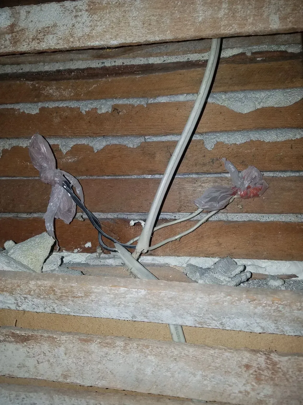 Electrical wires taped and exposed in a brick and wood structure.