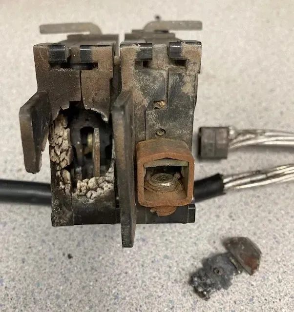 Damaged electrical circuit breaker, charred and melted, with exposed wires.