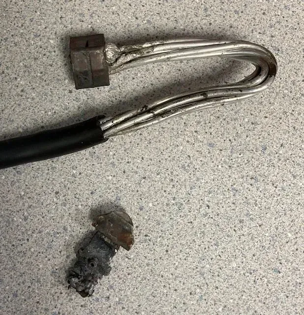 Damaged electrical cable with multiple exposed wires, metal nut, and debris on a gray surface.