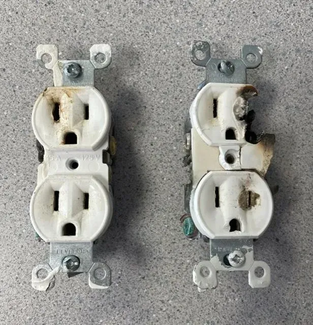 Two damaged electrical outlets with burn marks, mounted on a gray surface.