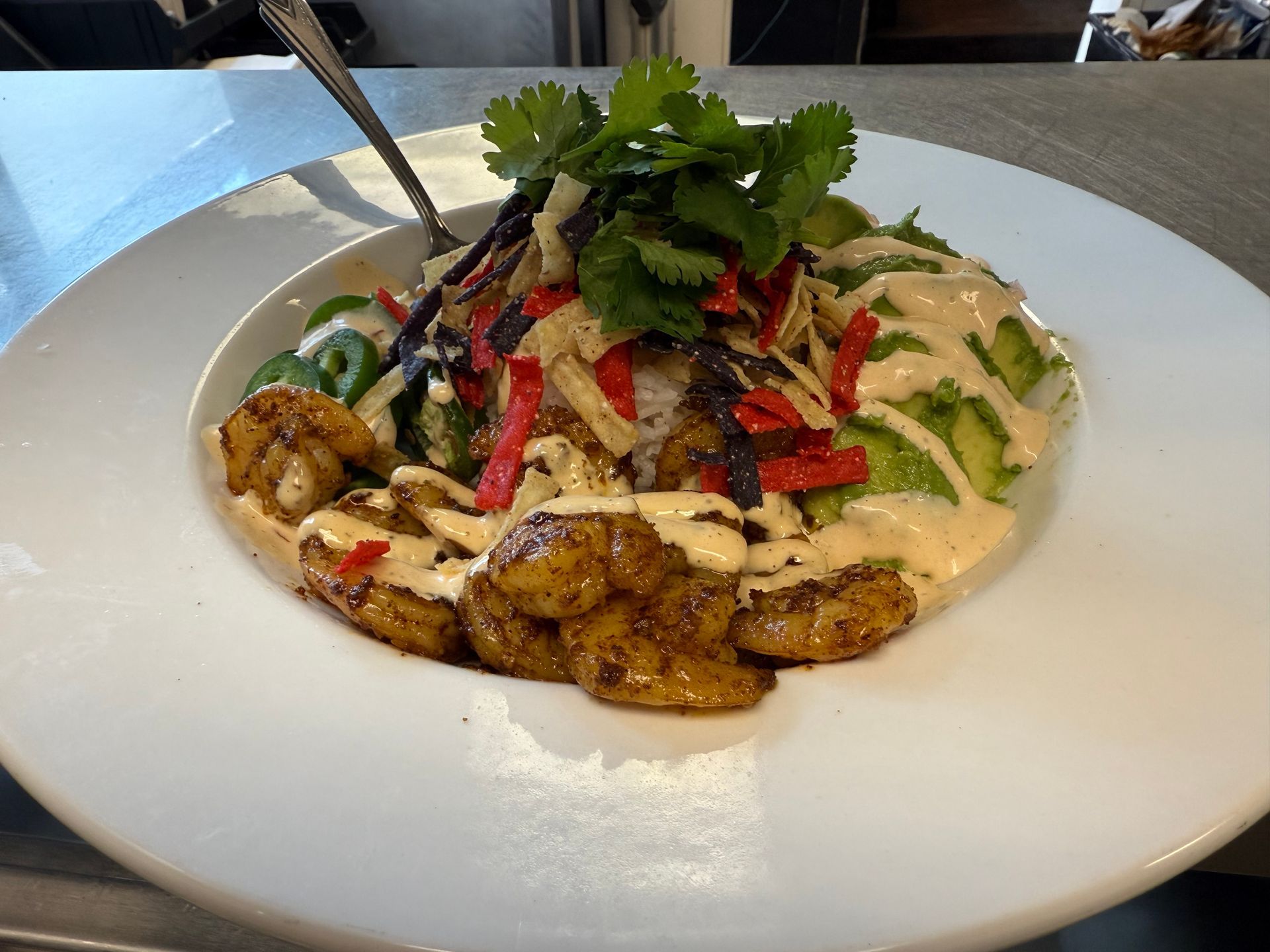 Shrimp bowl with avocado, cilantro, tortilla strips, and sauce on white plate.