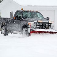 A truck is plowing snow in front of a garage.