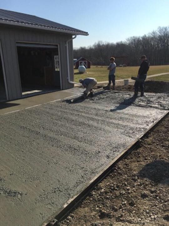 A group of people are working on a concrete driveway in front of a garage.