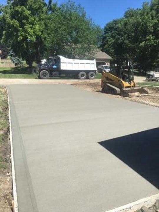 A dump truck is driving down a concrete driveway next to a bulldozer.