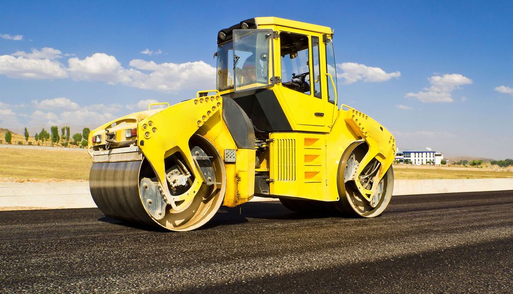 Yellow road roller on fresh asphalt at a construction site under a blue sky.