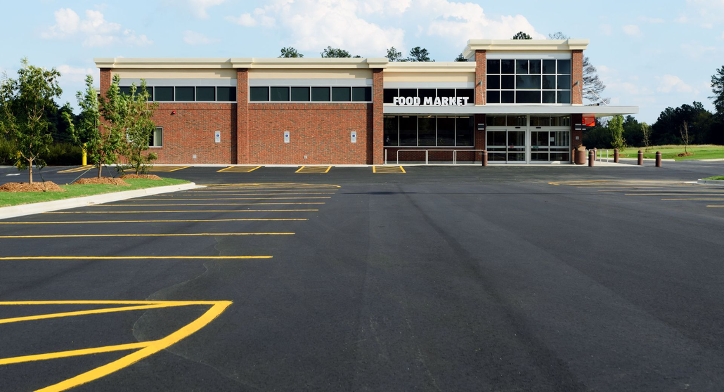 Empty parking lot in front of a brick building with a covered entrance and large windows