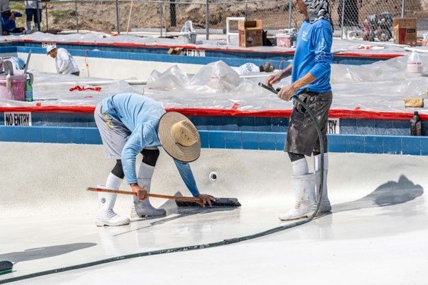A  pool installer is applying the interior finish to a newly build swimming pool