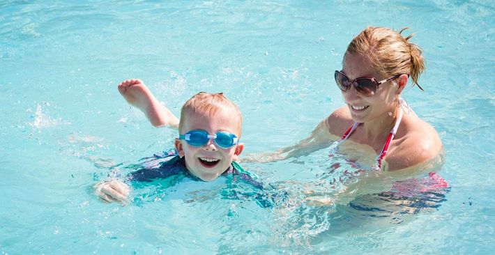 A woman is teaching a young boy how to swim in a swimming pool.