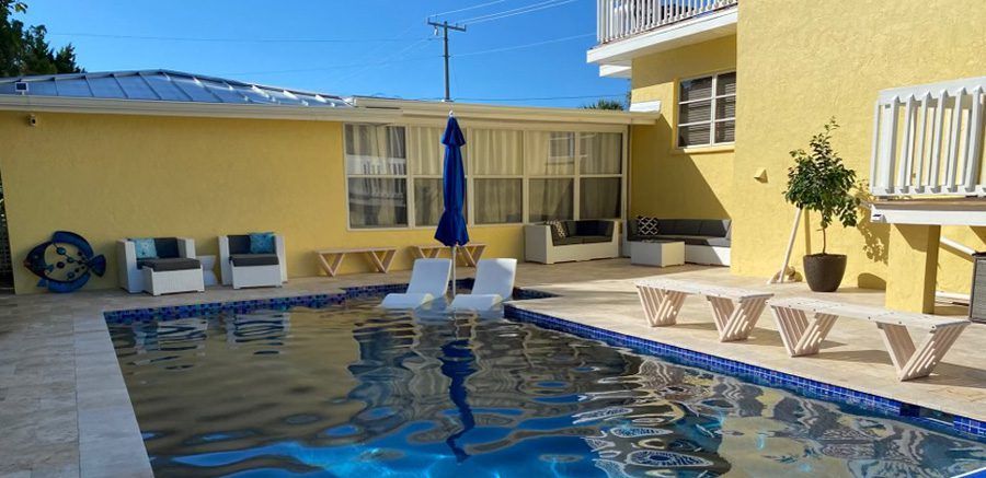 There is a large swimming pool in front of a yellow house.