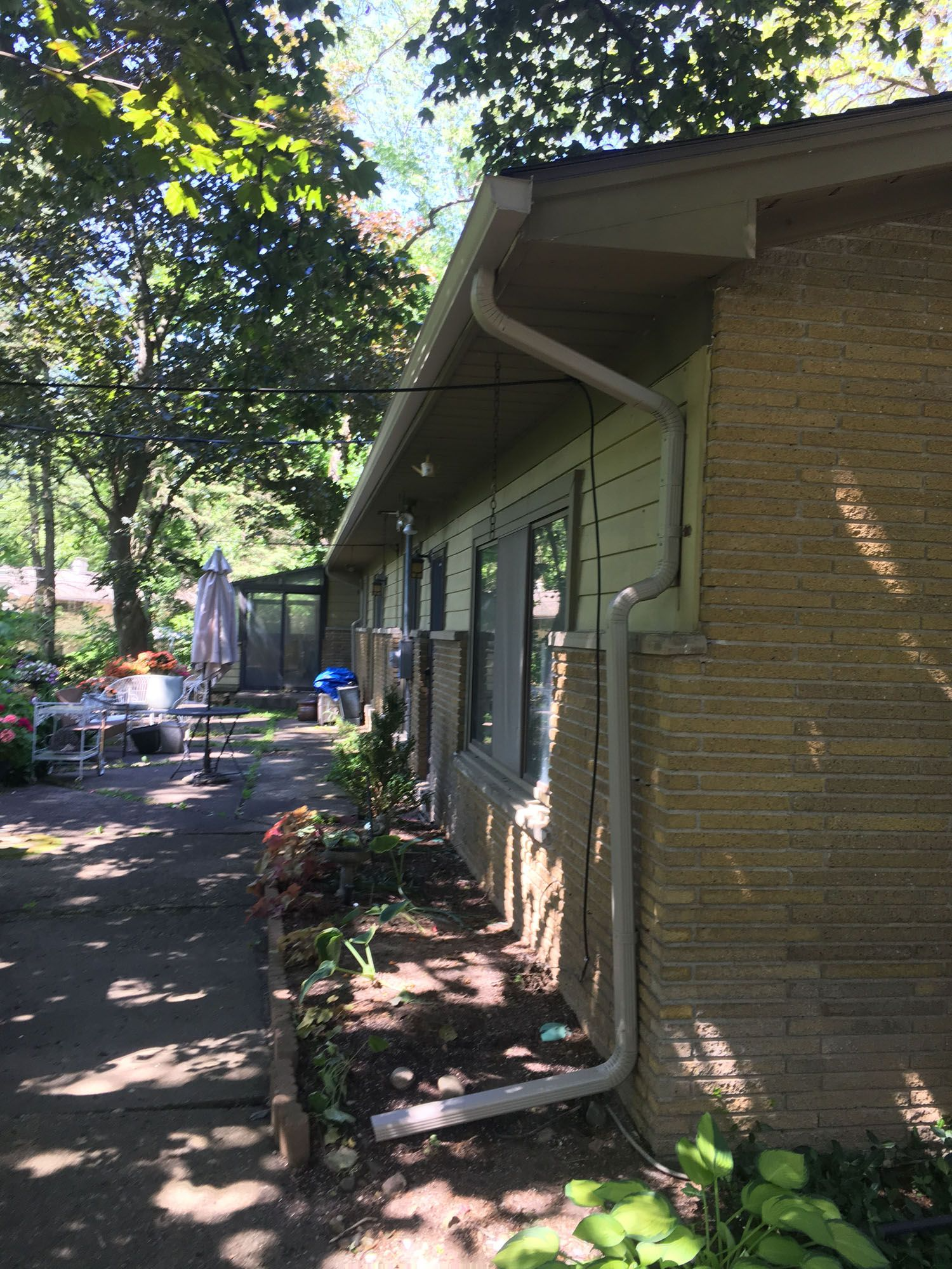 Exterior view of a house with a concrete block facade and a garden. White gutters run along the roofline.
