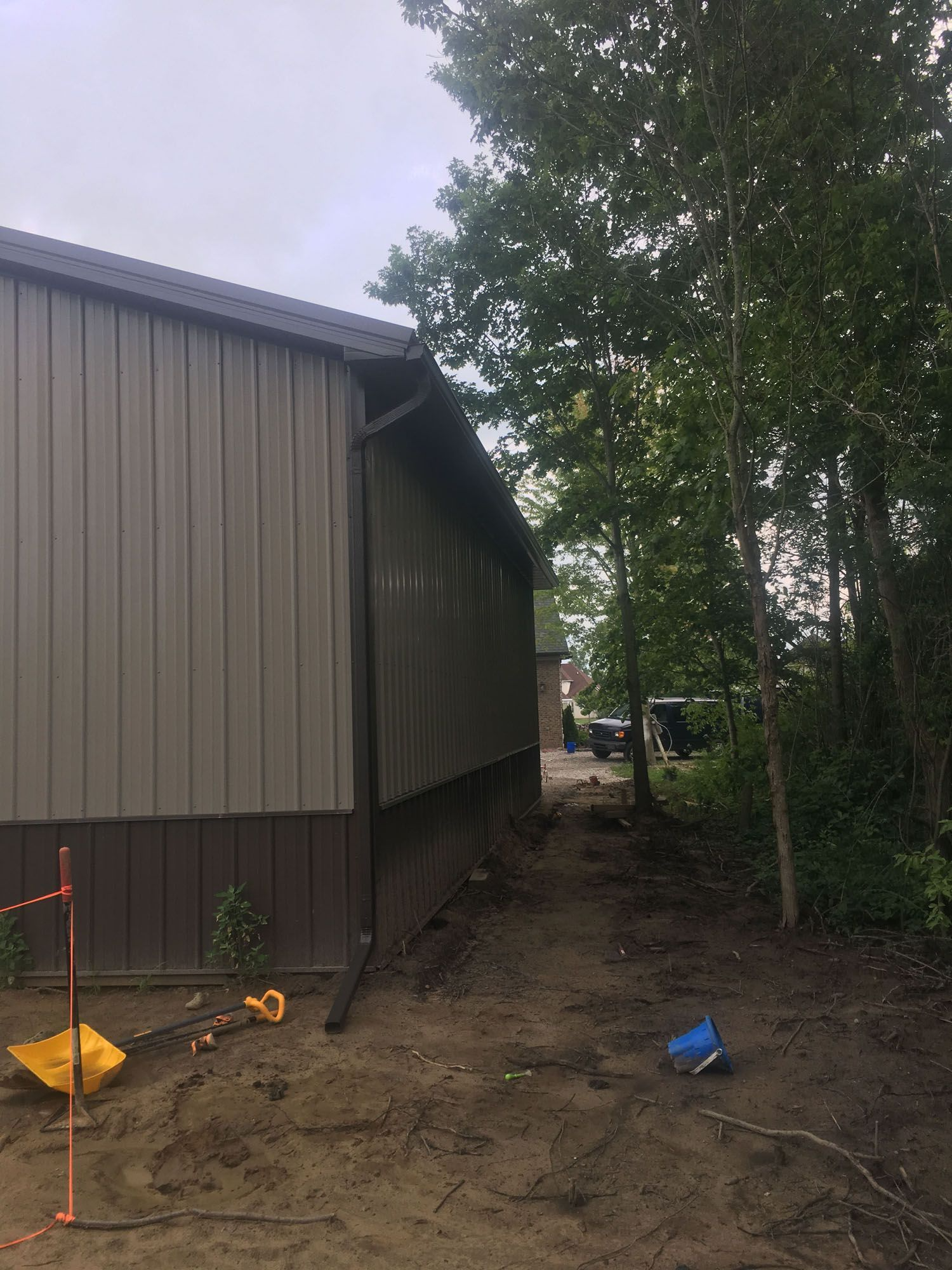 Side of a metal building with a dark brown base and tan walls. Gutter and trees are visible.