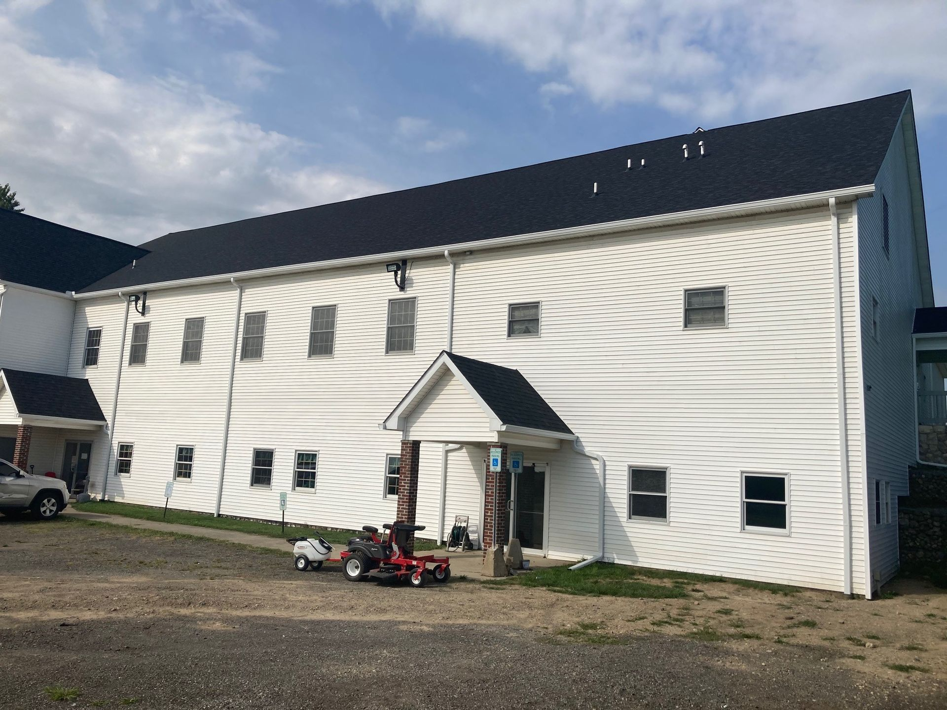 White two-story building with black roof, windows, and small entry porch. Landscaping equipment sits in the foreground.