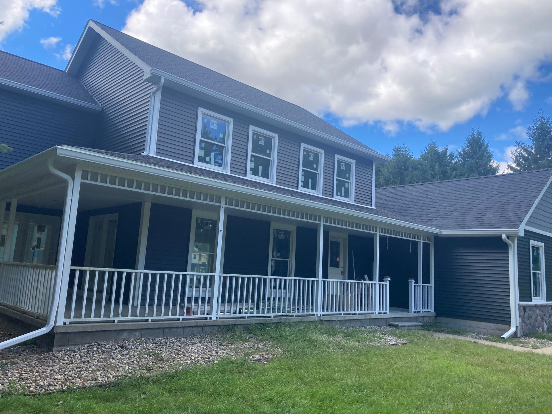 Dark blue house with white trim, porch, and railing, under a partly cloudy sky.