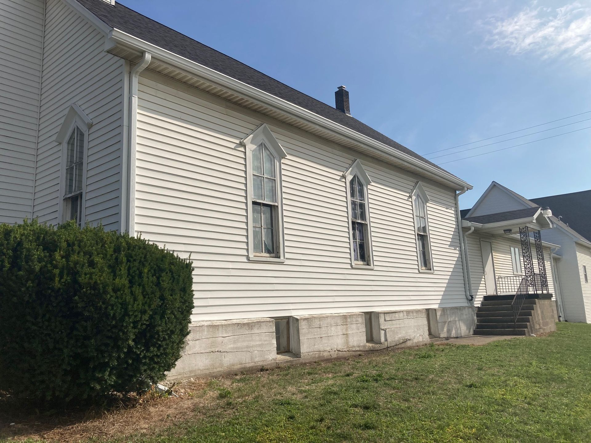 White clapboard church building with gothic-arched windows; blue sky background.