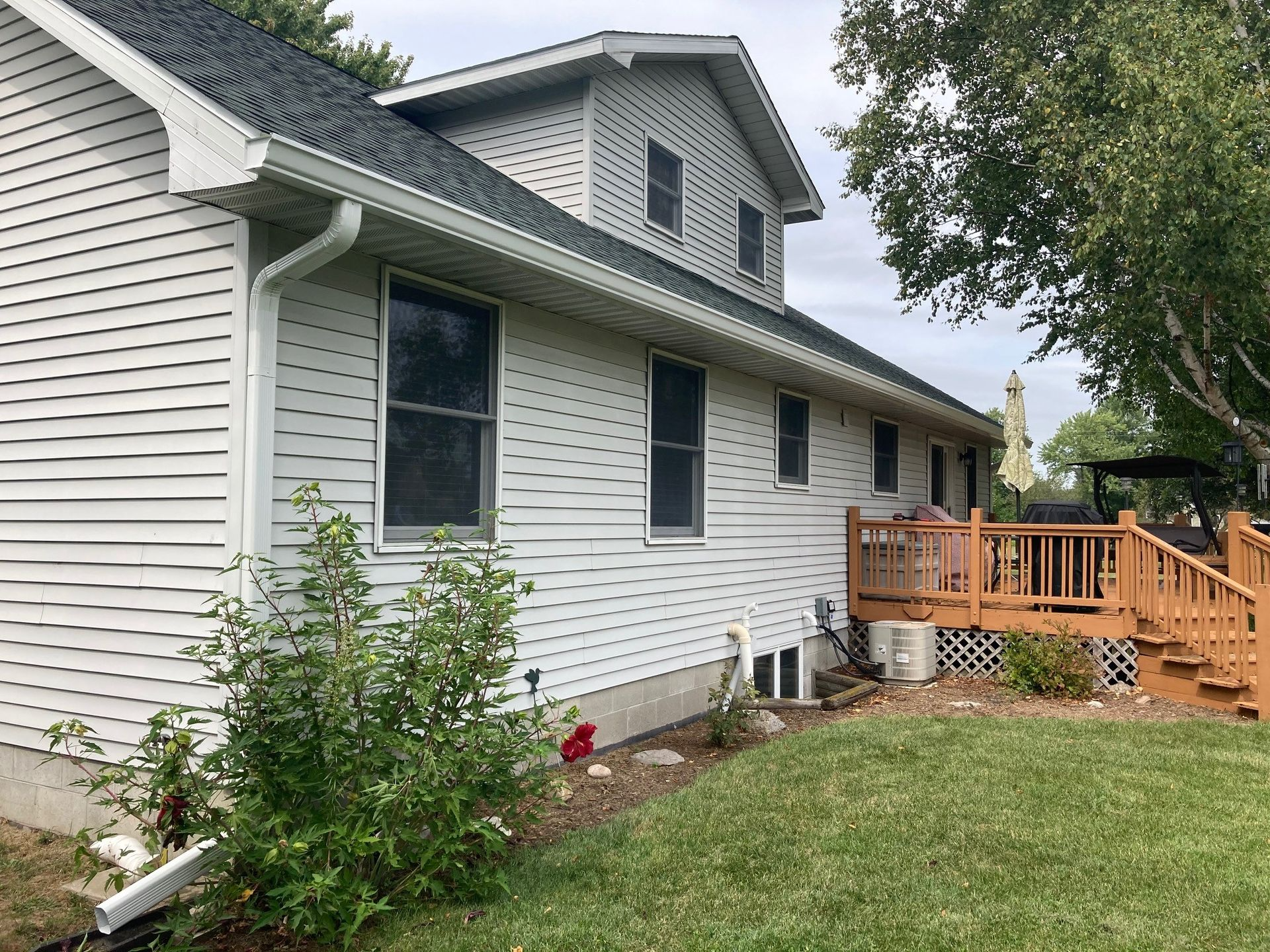 White house exterior with dark green roof, siding, windows, and wooden deck.