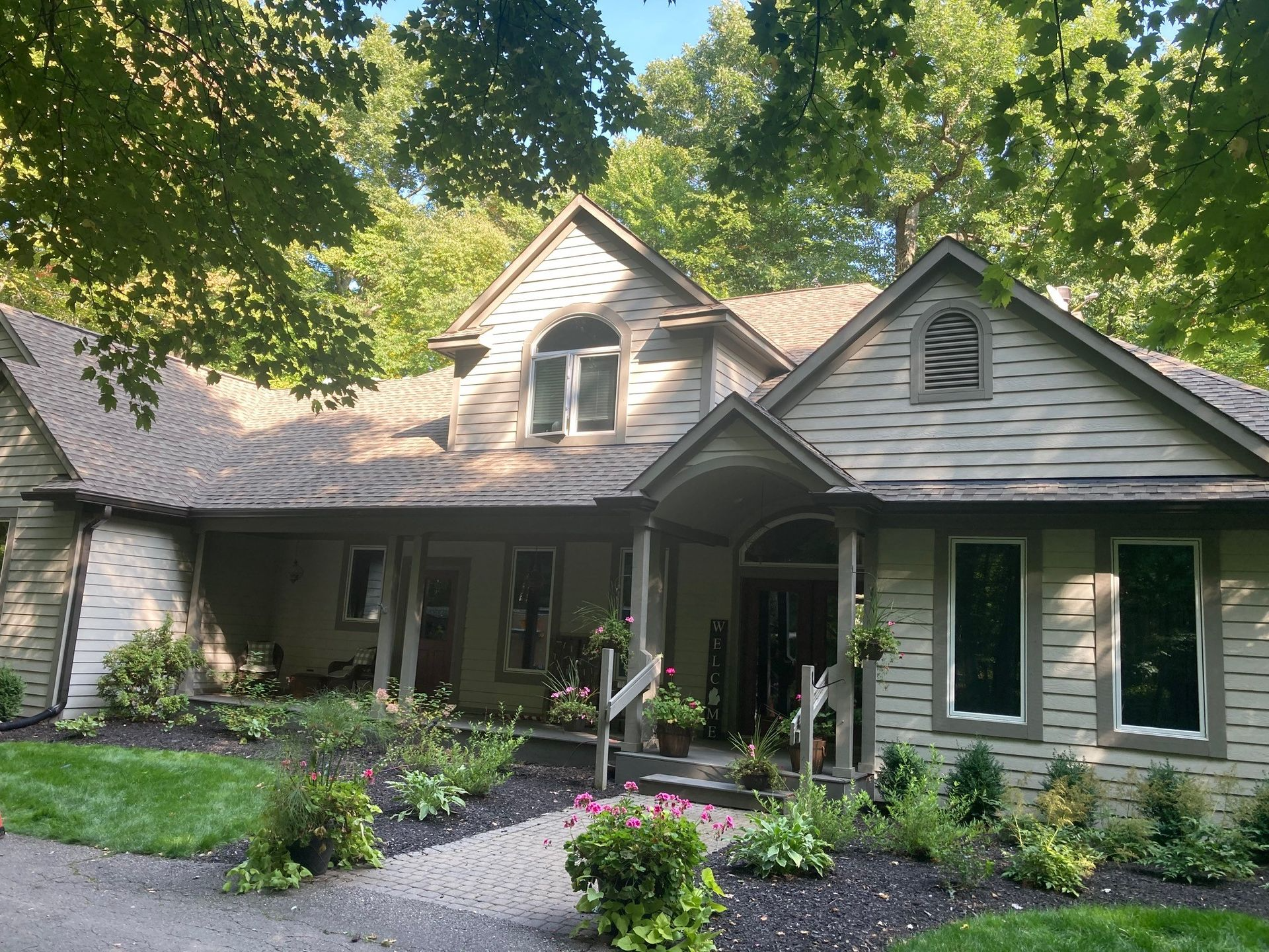 House with light brown siding, multiple gables, and a stone walkway. Surrounded by trees and landscaping.